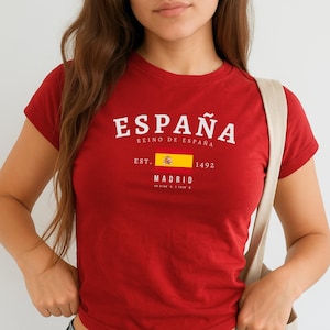 May include: A red cropped t-shirt with a white graphic print that says "ESPAÑA REINO DE ESPAÑA EST. 1492 MADRID" with a small image of the Spanish flag.