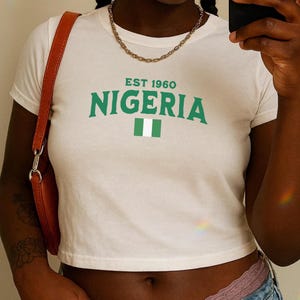 May include: White cropped t-shirt with a green graphic that says "EST 1960 NIGERIA" and a green and white flag.