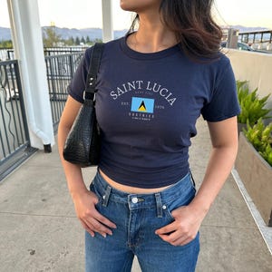 May include: A navy blue t-shirt with a white graphic of the flag of Saint Lucia and the text "Saint Lucia, East Caribbean, Est. 1979".