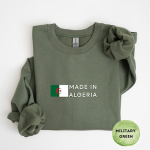 Könnte beinhalten: Militärgrünes Sweatshirt mit dem Text "MADE IN ALGERIA" und der algerischen Flagge. Das Sweatshirt hat einen Rundhalsausschnitt. Ein kreisförmiges Etikett unten rechts zeigt "MILITARY GREEN".