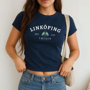 May include: Navy blue t-shirt with the text "LINKÖPING" in white, above the words "SWEDEN" and two crossed Swedish flags. The shirt also has the text "EST. 1120".