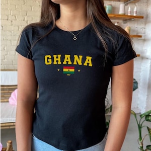 K&ouml;nnte beinhalten: Schwarzes T-Shirt mit einem gelben "GHANA"-Aufdruck und der ghanaischen Flagge mit dem Jahr "1957" darunter.