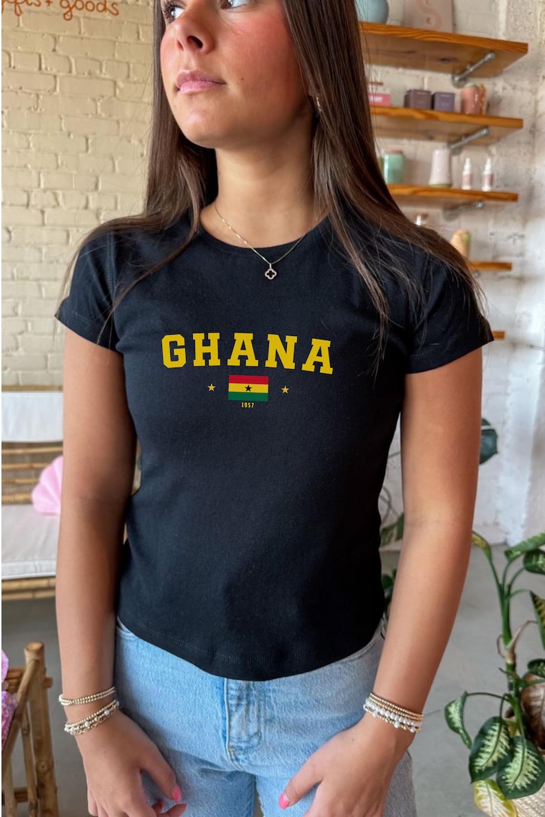 K&ouml;nnte beinhalten: Schwarzes T-Shirt mit einem gelben "GHANA"-Aufdruck und der ghanaischen Flagge mit dem Jahr "1957" darunter.