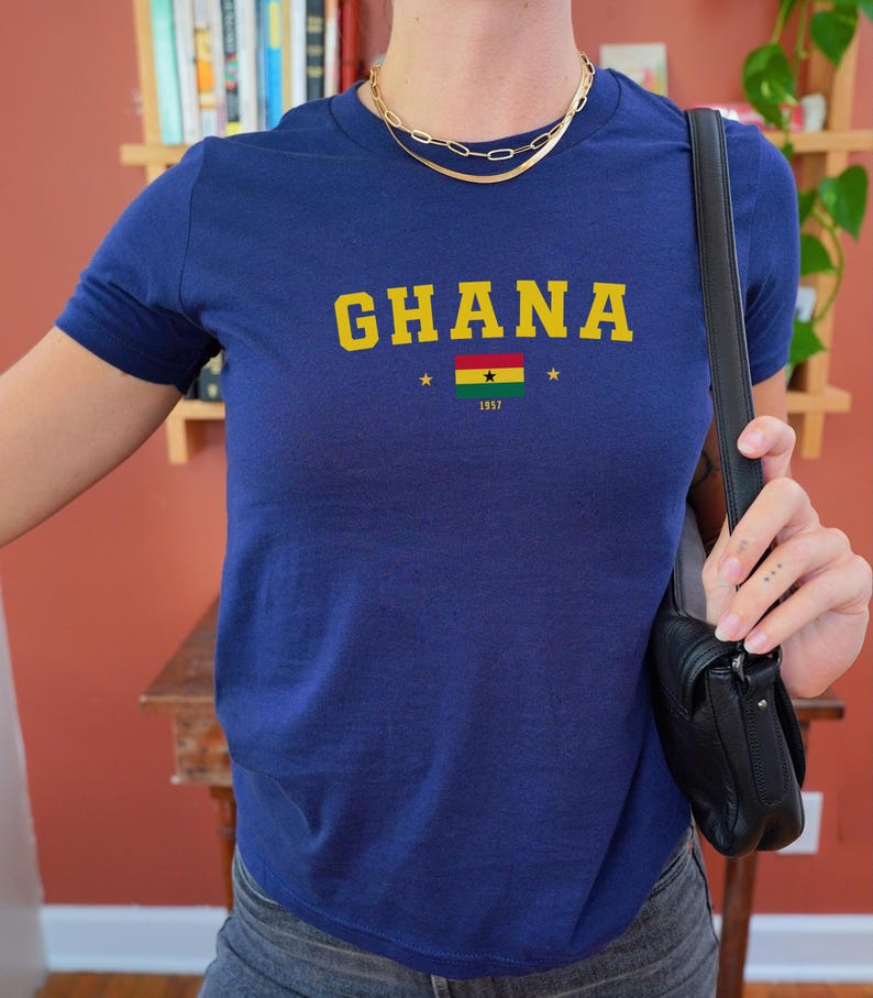 K&ouml;nnte beinhalten: Ein marineblaues T-Shirt mit dem Wort "GHANA" in gelben Buchstaben und einer kleinen ghanaischen Flagge mit dem Jahr "1957" darunter.