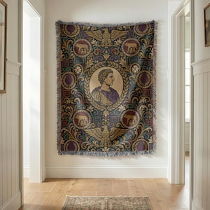 May include: A woven throw blanket featuring a central circular portrait of a Roman emperor in profile, surrounded by ornate gold, purple, and blue acanthus leaf patterns, eagles, and medallions depicting the she-wolf with Romulus and Remus.