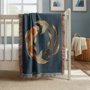 May include: A dark blue woven throw blanket featuring a circular graphic of two koi fish in a yin-yang formation. One fish is orange and white, while the other is black and white. The blanket has a decorative fringed edge on all four sides.