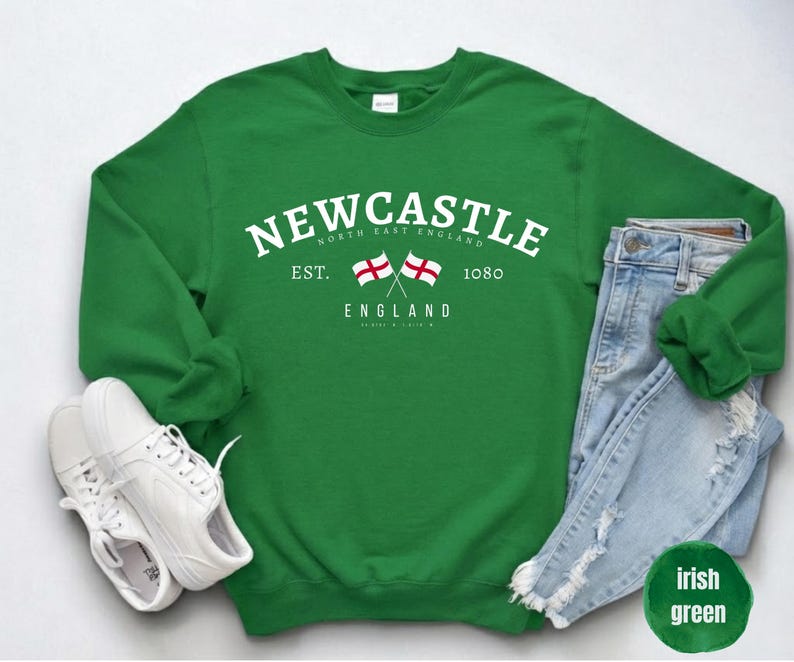 Puede incluir: Sudadera verde irlandesa con la palabra "Newcastle" en texto blanco, con dos banderas cruzadas y el texto "England". La sudadera se combina con vaqueros de lavado claro y zapatillas blancas. El texto "North East England" tambi&eacute;n es visible.