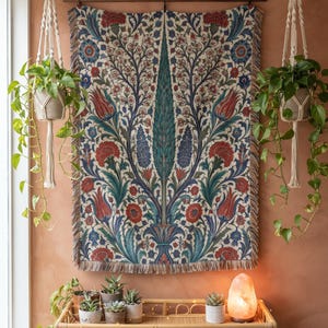 May include: A rectangular woven wall tapestry featuring a symmetrical botanical pattern with red tulips, blue floral motifs, and green foliage on a cream background, finished with a fringed bottom edge and suspended from a dark wooden rod.