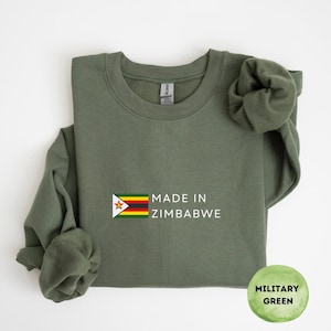 Könnte beinhalten: Militärgrünes Sweatshirt mit dem Text "MADE IN ZIMBABWE" und der simbabwischen Flagge. Das Sweatshirt hat einen Rundhalsausschnitt und lange Ärmel. Ein kreisförmiges Etikett unten rechts zeigt "MILITARY GREEN".