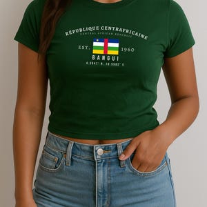 May include: A green t-shirt with a white graphic print of the Central African Republic flag and the text "REPUBLIQUE CENTRAFRICAINE CENTRAL AFRICAN REPUBLIC EST. 1960 BANGUI 4.3947° N, 18.5582° E"