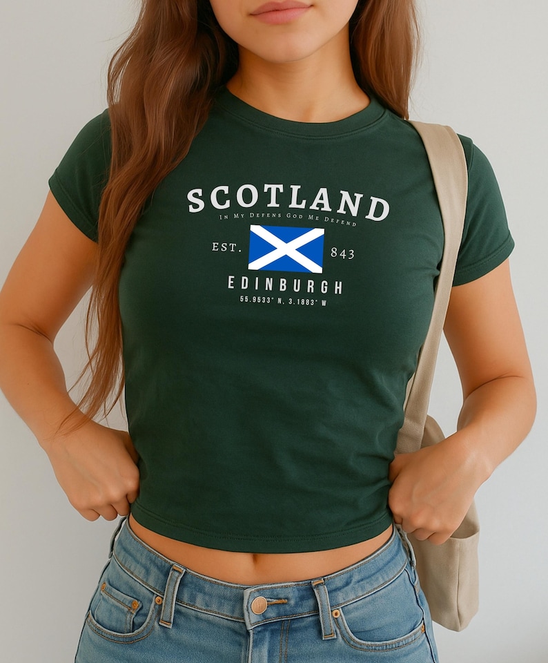 May include: Dark green crop top with the word "SCOTLAND" in white arched text. Below is a white and blue flag, the text "EDINBURGH" and coordinates. The text "In My DEFENS GOD ME DEFEND" is above the word "SCOTLAND".