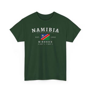 Puede incluir: Camiseta verde oscuro con la palabra "NAMIBIA" sobre la bandera de Namibia y el texto "REPUBLIC OF NAMIBIA", "EST. 1990" y "WINDHOEK" con coordenadas. La camiseta es de color liso.