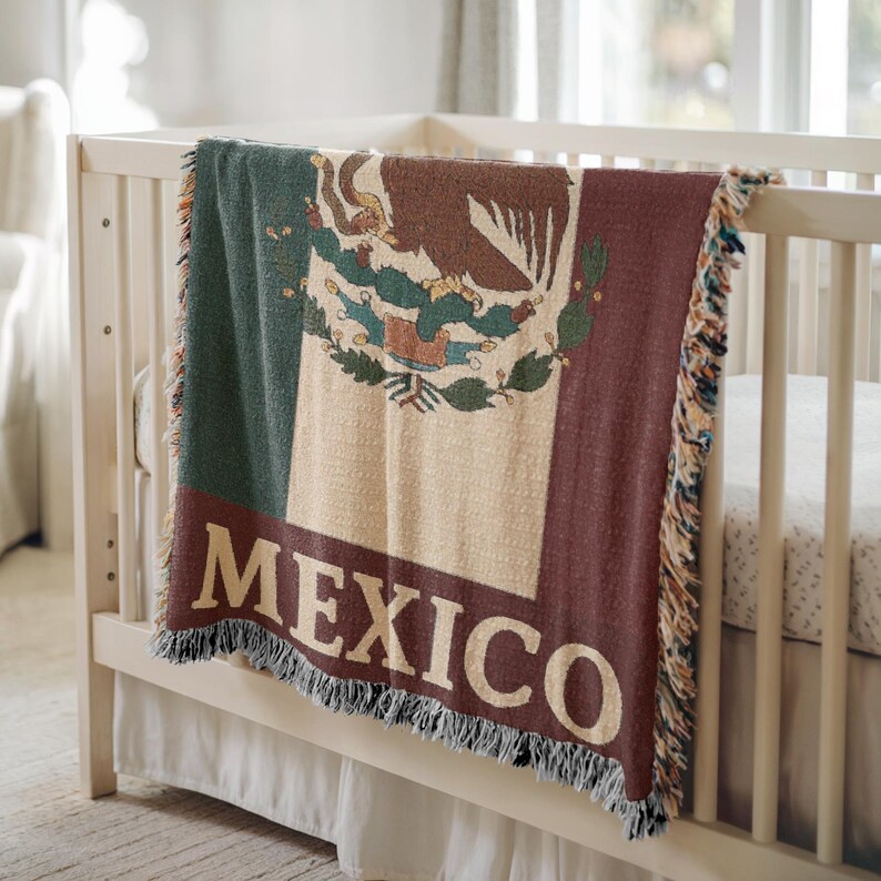May include: A woven blanket draped over a crib, featuring the Mexican flag design. The blanket displays the colors green, white, and red, with the Mexican coat of arms in the center. The word "MEXICO" is prominently displayed in large, white letters at the bottom.