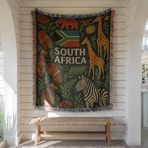 以下が含まれることがあります： 暗い背景に「SOUTH AFRICA」の文字、南アフリカの国旗、2頭のキリン、シマウマ、ゾウ、ターバンを巻いた2人の人物、2つの部族の仮面、植物が描かれた織物のスローケットで、縁にはフリンジがあしらわれています。
