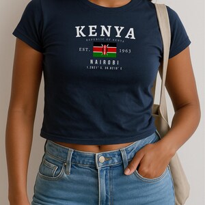 May include: A navy blue cropped t-shirt with a white graphic print of the Kenyan flag and the text "KENYA REPUBLIC OF KENYA EST. 1963 NAIROBI 1.2921&deg; S, 36.8219&deg; E"