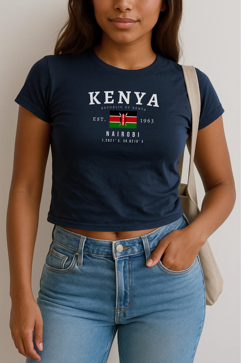 May include: A navy blue cropped t-shirt with a white graphic print of the Kenyan flag and the text "KENYA REPUBLIC OF KENYA EST. 1963 NAIROBI 1.2921&deg; S, 36.8219&deg; E"
