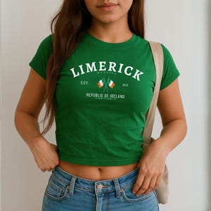 May include: A green crop top with the word "LIMERICK" in white arched across the chest, with "MUNSTER" above it. Below the word "LIMERICK" are two crossed Irish flags and the text "EST. 915 REPUBLIC OF IRELAND".