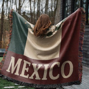 May include: A woven blanket featuring the colors of the Mexican flag: green, white, and red. The word "MEXICO" is prominently displayed in large, white letters. The blanket has a fringed edge and a detailed emblem.