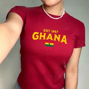 May include: A red t-shirt with a yellow graphic that says "EST 1957 GHANA" and a small Ghanaian flag.