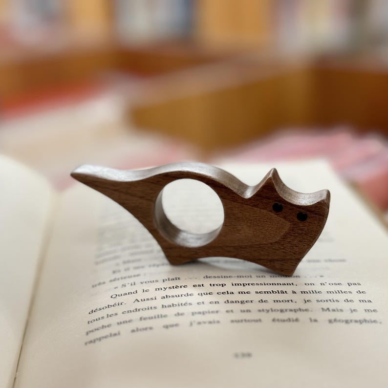 May include: A wooden cat-shaped bookend with a ring for holding pages. The bookend is brown and has a natural wood finish.