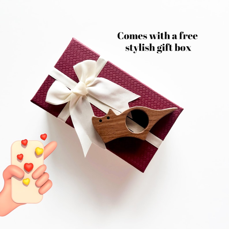 May include: A wooden cat-shaped bookmark with a ring for holding a page. The bookmark is in a red gift box with a white ribbon. The text "Comes with a free stylish gift box" is above the box.