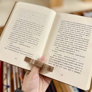 May include: A close-up of an open book with a wooden page holder. The book is open to a page with text about a man who is lost and a drawing of a sheep. The text reads "S'il vous pla&icirc;t... dessine-moi un mouton..."
