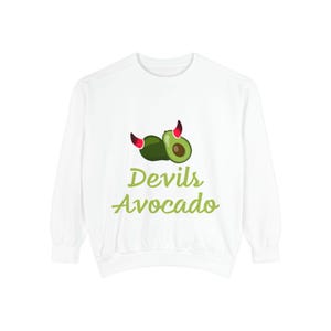 May include: White sweatshirt featuring a green avocado with red devil horns and the text "Devils Avocado" in green. The avocado is cut open, revealing a green interior and a brown pit. The sweatshirt has long sleeves.