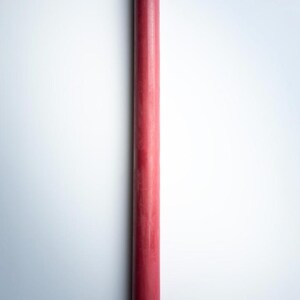 May include: A tall, slender, red taper candle. The candle has a pointed top with a small, white wick. The body of the candle is a solid, matte red color. The candle is a classic design, suitable for various decorative purposes.