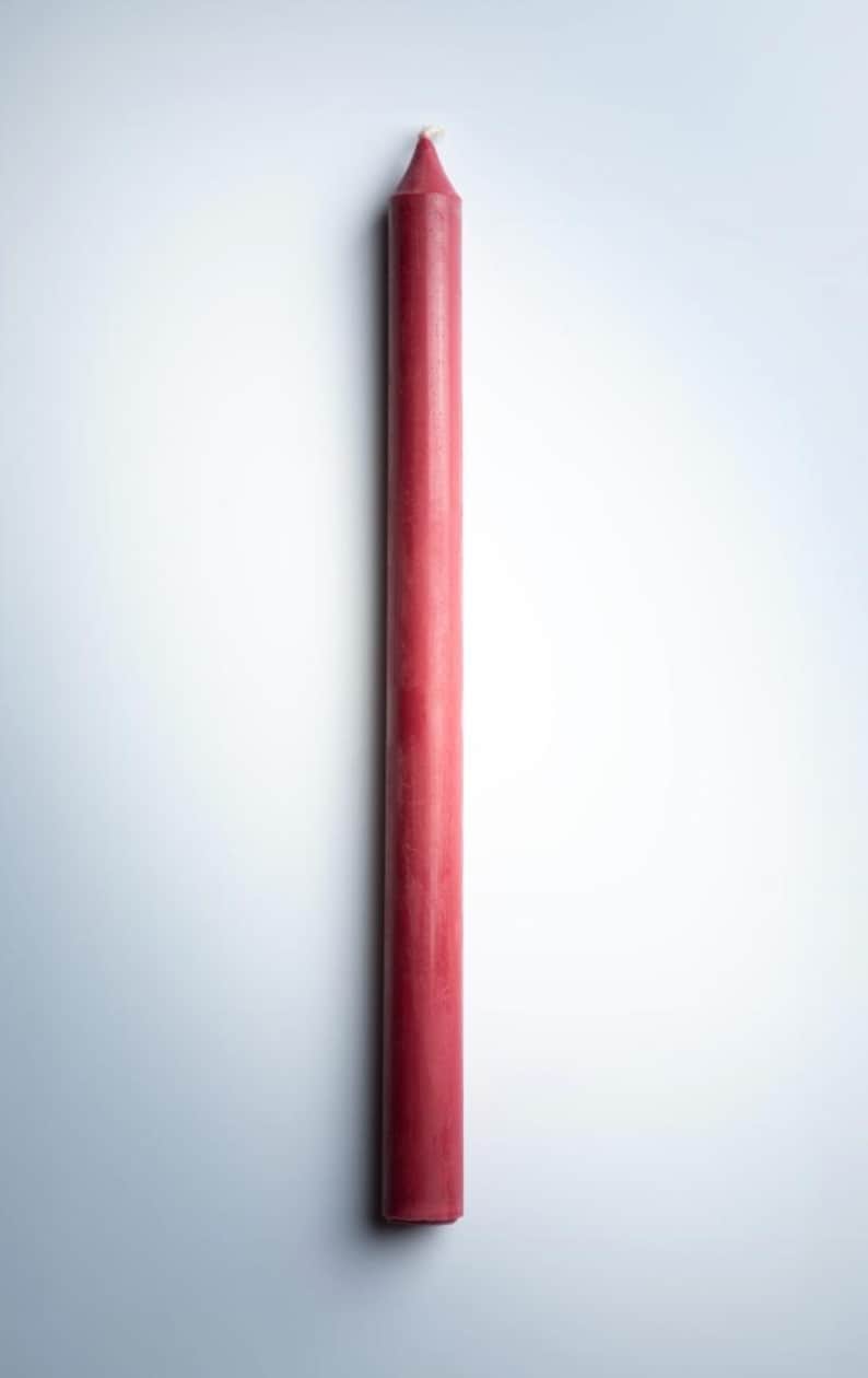 May include: A tall, slender, red taper candle. The candle has a pointed top with a small, white wick. The body of the candle is a solid, matte red color. The candle is a classic design, suitable for various decorative purposes.