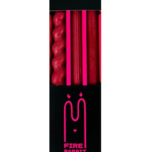 May include: A black box containing red candles of various shapes. The box features the text "FIRE RABBIT" in pink, along with a rabbit logo. The candles are arranged vertically, with a twisted candle on the left.
