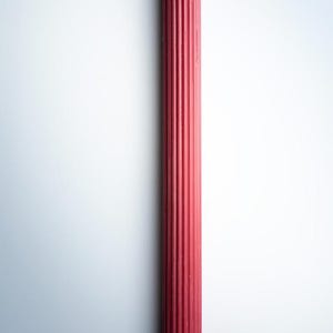 May include: A tall, red pillar candle with a ribbed design. The candle has a simple, elegant form and a wick at the top. The candle is a deep red color and is set against a white background.