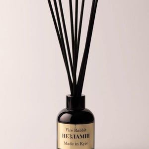 May include: A black glass diffuser bottle with black reeds. The bottle has a gold label with the text "Fire Rabbit НЕЗЛАМНІ Made in Kyiv". The base of the bottle is a teal color.