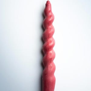 May include: A tall, spiral-shaped candle in a deep rose color. The candle has a twisted design, with a wick at the top. The candle is a decorative item, suitable for home decor or special occasions.