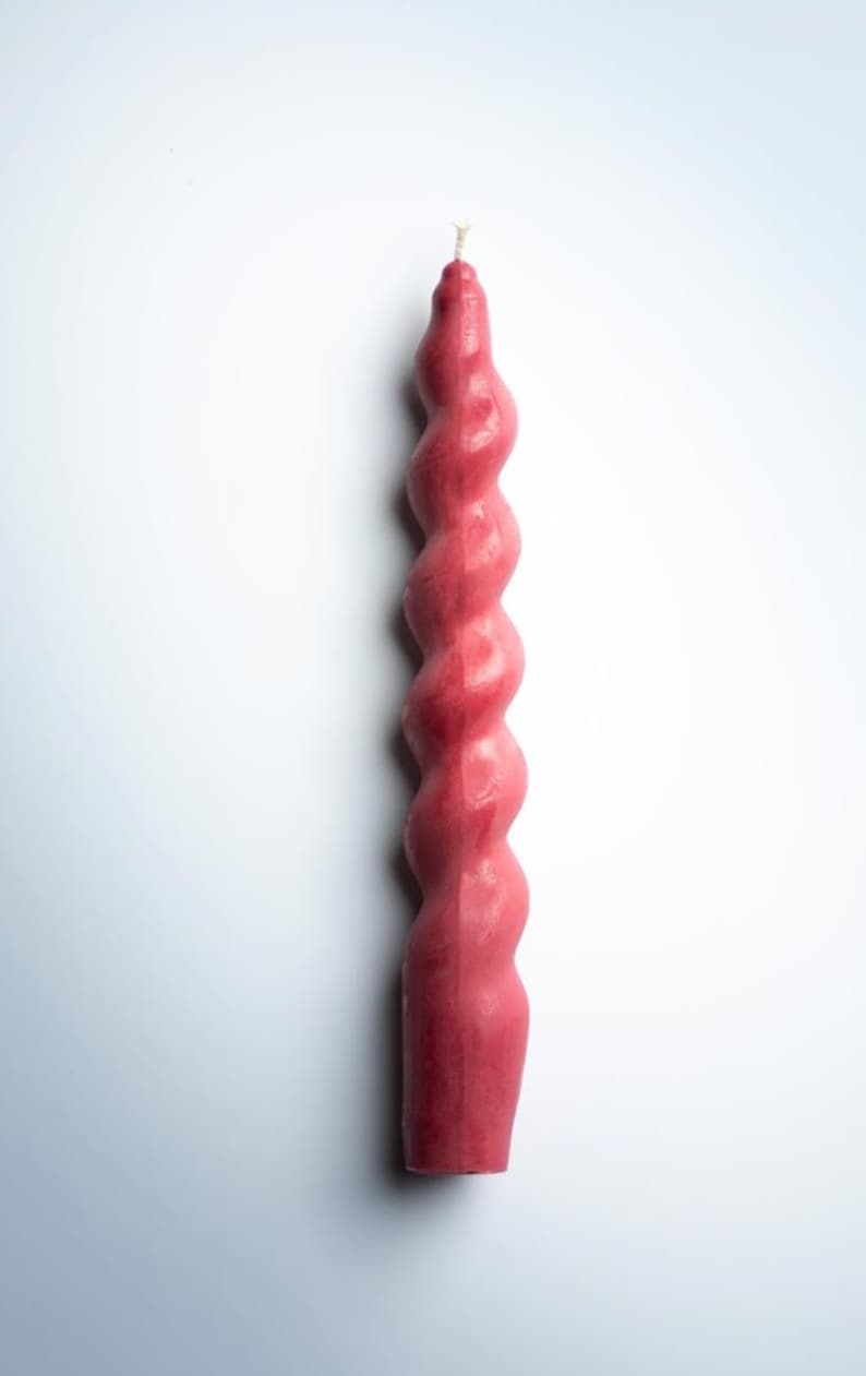 May include: A tall, spiral-shaped candle in a deep rose color. The candle has a twisted design, with a wick at the top. The candle is a decorative item, suitable for home decor or special occasions.