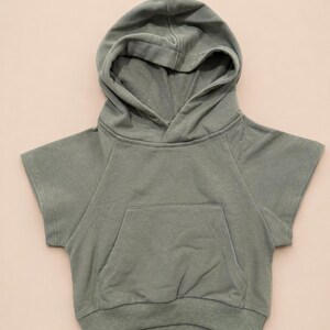 May include: Sage green hooded sweatshirt with short sleeves and a front pocket. The sweatshirt has a drawstring hood and ribbed hem. This casual top is perfect for everyday wear.