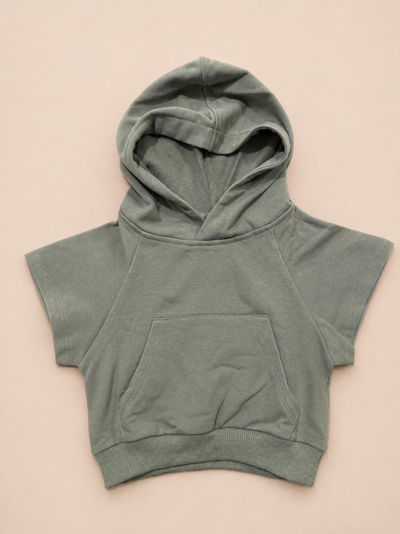 May include: Sage green hooded sweatshirt with short sleeves and a front pocket. The sweatshirt has a drawstring hood and ribbed hem. This casual top is perfect for everyday wear.