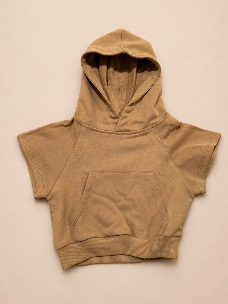 May include: A tan-colored hooded sweatshirt with short sleeves. The sweatshirt features a front pocket and a ribbed hem. The hood is lined and the garment is made of a soft, comfortable material. This casual top is suitable for children.