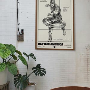 May include: Black and white illustration of Captain America throwing his shield. The image includes quotes from Captain America, including "I'm just a kid from Brooklyn" and "The price of freedom is a price I'm willing to pay."
