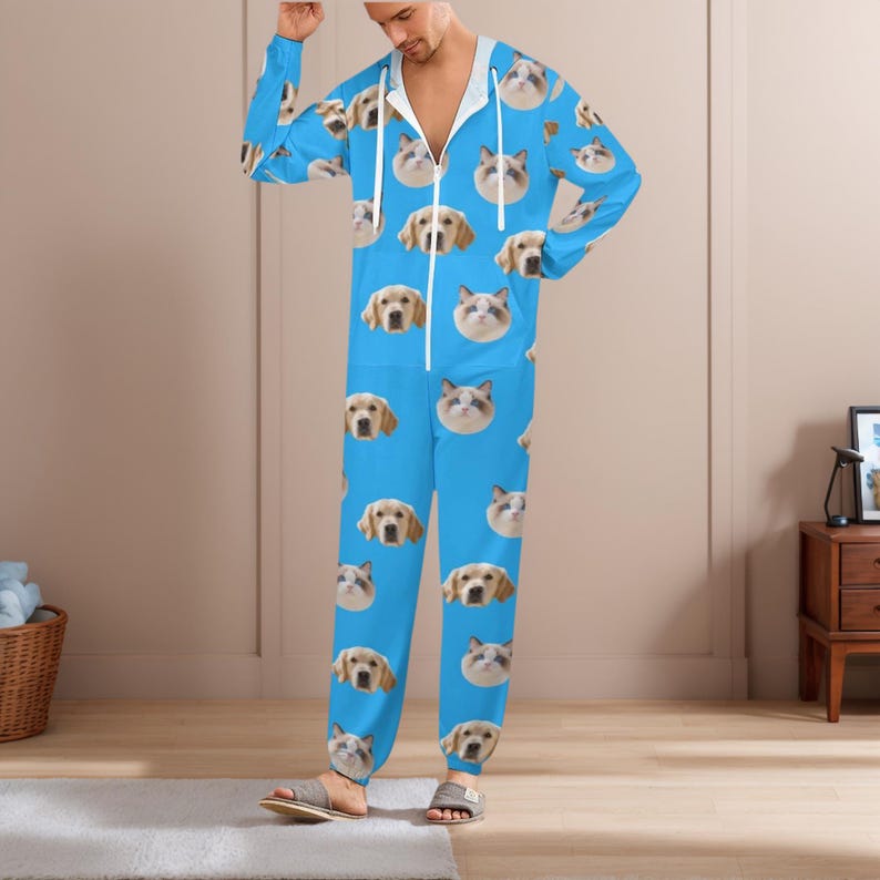 May include: A blue hooded jumpsuit featuring a repeating pattern of dog and cat faces. The jumpsuit has a white zipper and drawstring. The model is wearing gray sandals.