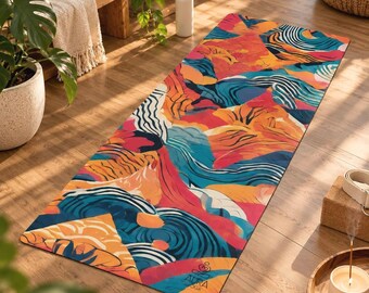May include: A rectangular yoga mat featuring a vibrant abstract pattern of swirling orange, pink, teal, and dark blue shapes. The mat displays the Aura Yoga logo printed in black near the bottom edge on a smooth, flat surface.