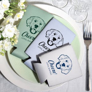 May include: Three beverage insulators in shades of green, blue, and white, each featuring a dog illustration and the word "Cheers!" with "Love, Ravioli" below. The insulators are arranged on a plate with a fork.