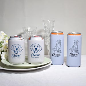 May include: Four beverage can coolers. Two are white with a blue dog face and the text "Cheers! Love, Ravioli". The other two are light blue with a dog illustration and the text "Cheers! Love, Joey".