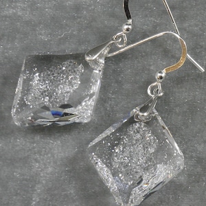 May include: A pair of silver dangle earrings with clear crystal square-shaped stones. The stones have a textured, sparkly finish.