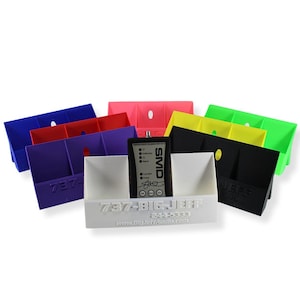 May include: A collection of colorful plastic organizers in blue, red, purple, pink, yellow, green, black, and white. Each organizer has three compartments and a hole. A black device with the text "SMD" is in the white organizer.