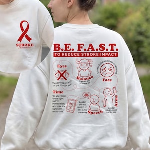 May include: White sweatshirt with red text and graphics promoting stroke awareness. The front features a red ribbon and the words "STROKE Awareness." The back displays "B.E. F.A.S.T." and a diagram explaining stroke symptoms, including vision, balance, face, arms, and speech.