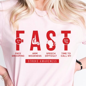 May include: Pink t-shirt with the word "FAST" in red letters. Each letter has a symbol representing a stroke symptom: a sad face for face drooping, a raised arm for arm weakness, a person talking for speech difficulty, and a phone for calling 911. The text "STROKE AWARENESS" is below the letters.