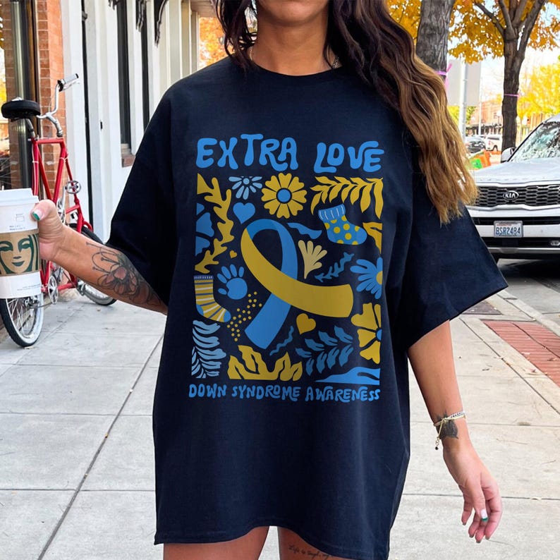 A Down Syndrome Awareness T-shirt with “3:21” and “Extra Love” printed in a heart-themed design. The unisex shirt represents support for the Down syndrome community and T21 families. Made of durable cotton with a relaxed fit, ideal for events, family gatherings, or spreading awareness every day.