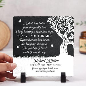 May include: A black and white memorial plaque with a tree design and the text "A limb has fallen from the family tree." The plaque includes the name Robert Miller and dates April 22, 1955 - May 15, 2025.