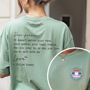 May include: Sage green t-shirt with text that reads "Dear person, It doesn't matter your race, your gender, your legal status, who you pray to, or who you love you're safe with me. Love a fellow human." A small graphic is also present.