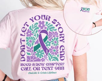 May include: Pink t-shirt with a purple ribbon and floral design on the back. The text reads "Don't let your story end. Need a new chapter? Call or text 988 (Suicide & Crisis Lifeline)". The front of the shirt has a purple ribbon with the text "You matter".